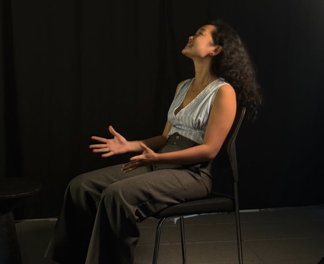 Amelia Ali performing a seated monologue on stage